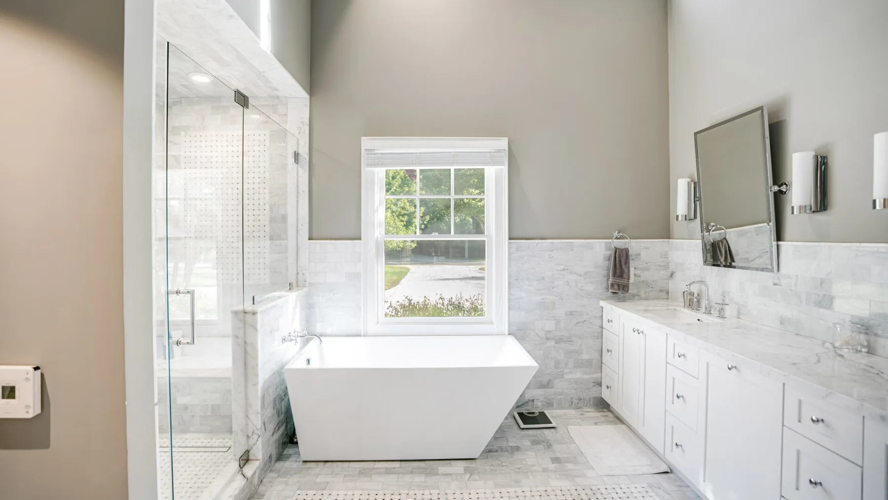 A bright bathroom with a freestanding bathtub, glass shower, and long vanity.