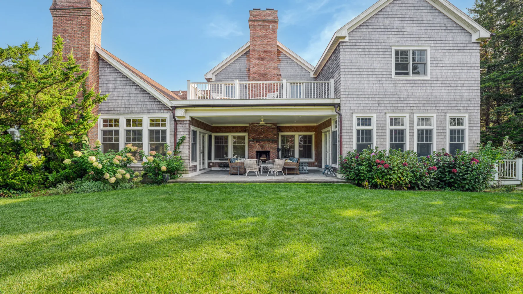 A large gray house with a covered patio opens onto a green lawn.