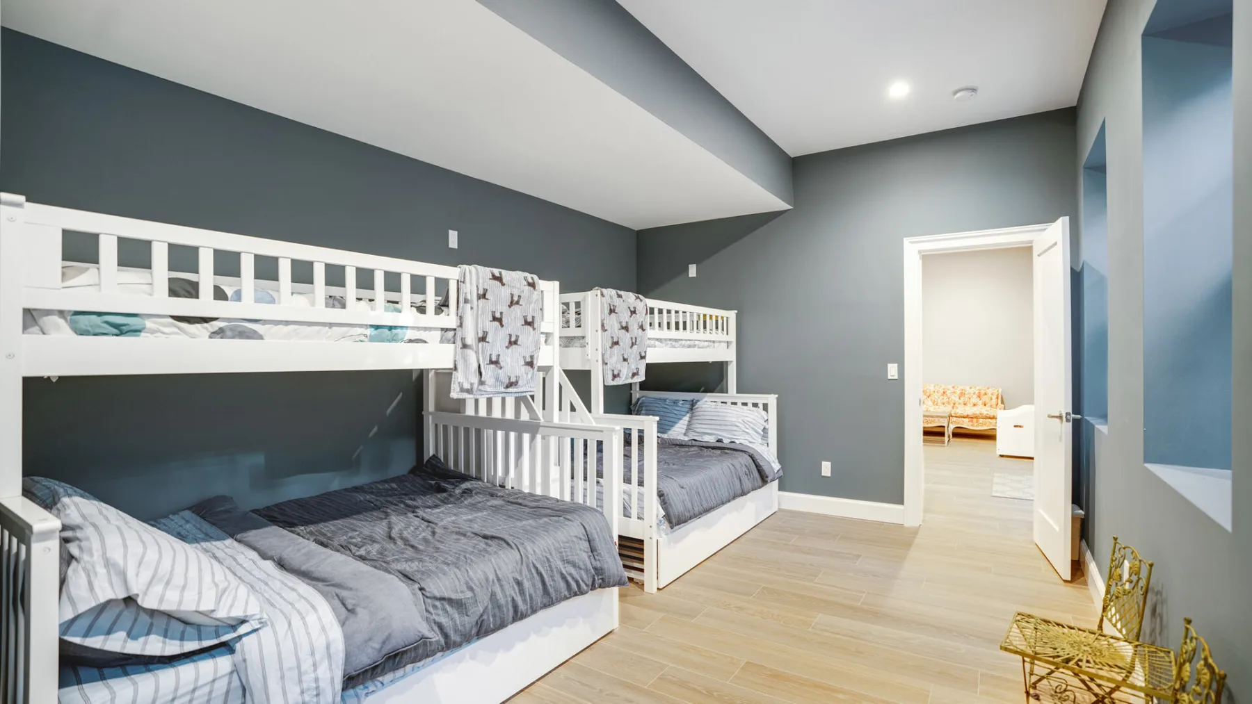 A bedroom with white bunk beds, gray bedding, and an open doorway.
