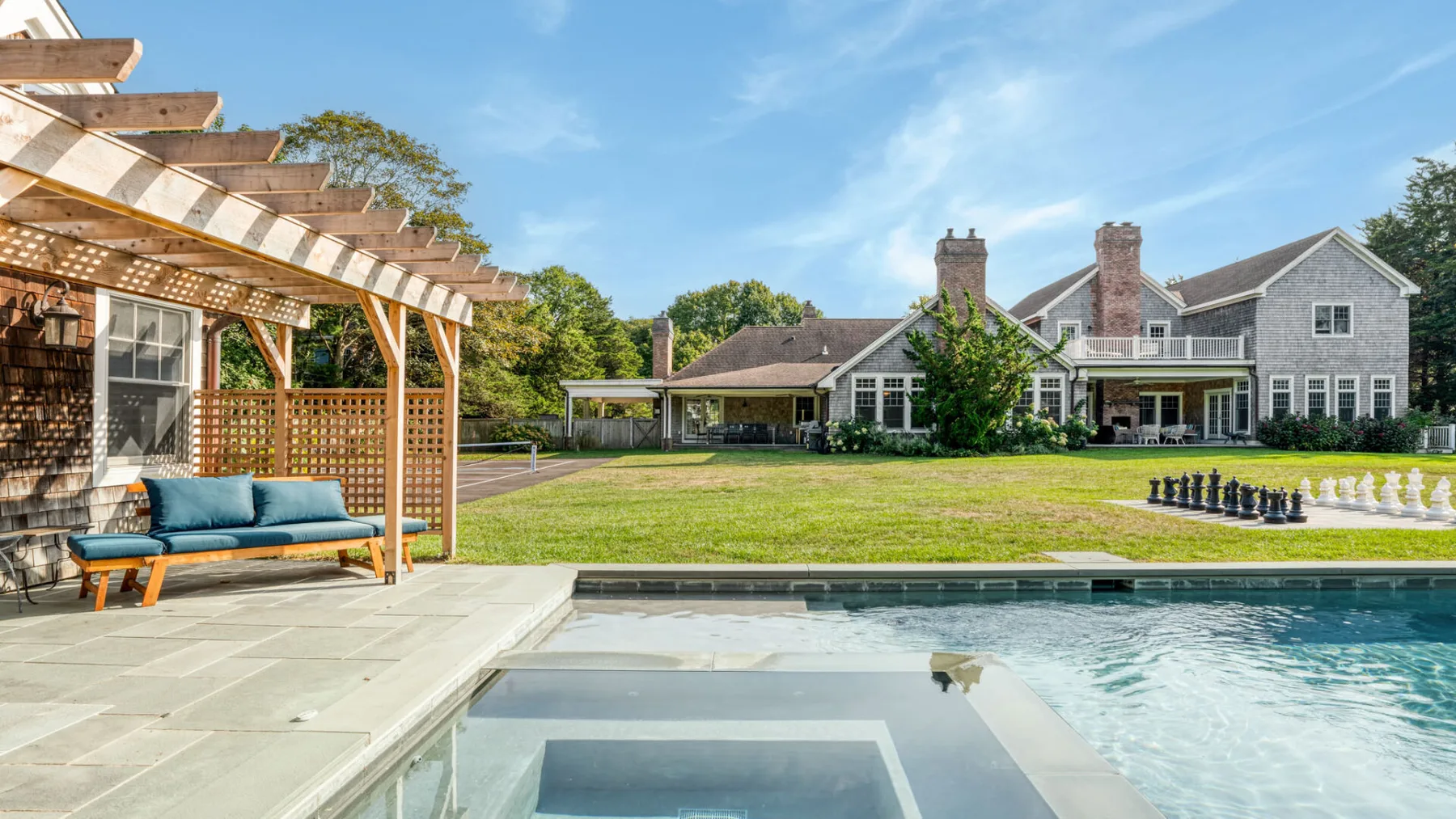 A large house overlooks a lawn, patio, and outdoor pool.