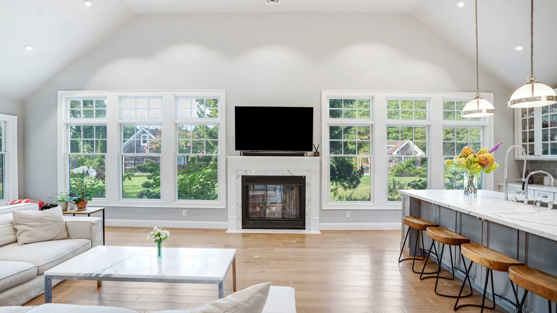 A bright open-plan living and kitchen area has large windows and a fireplace.