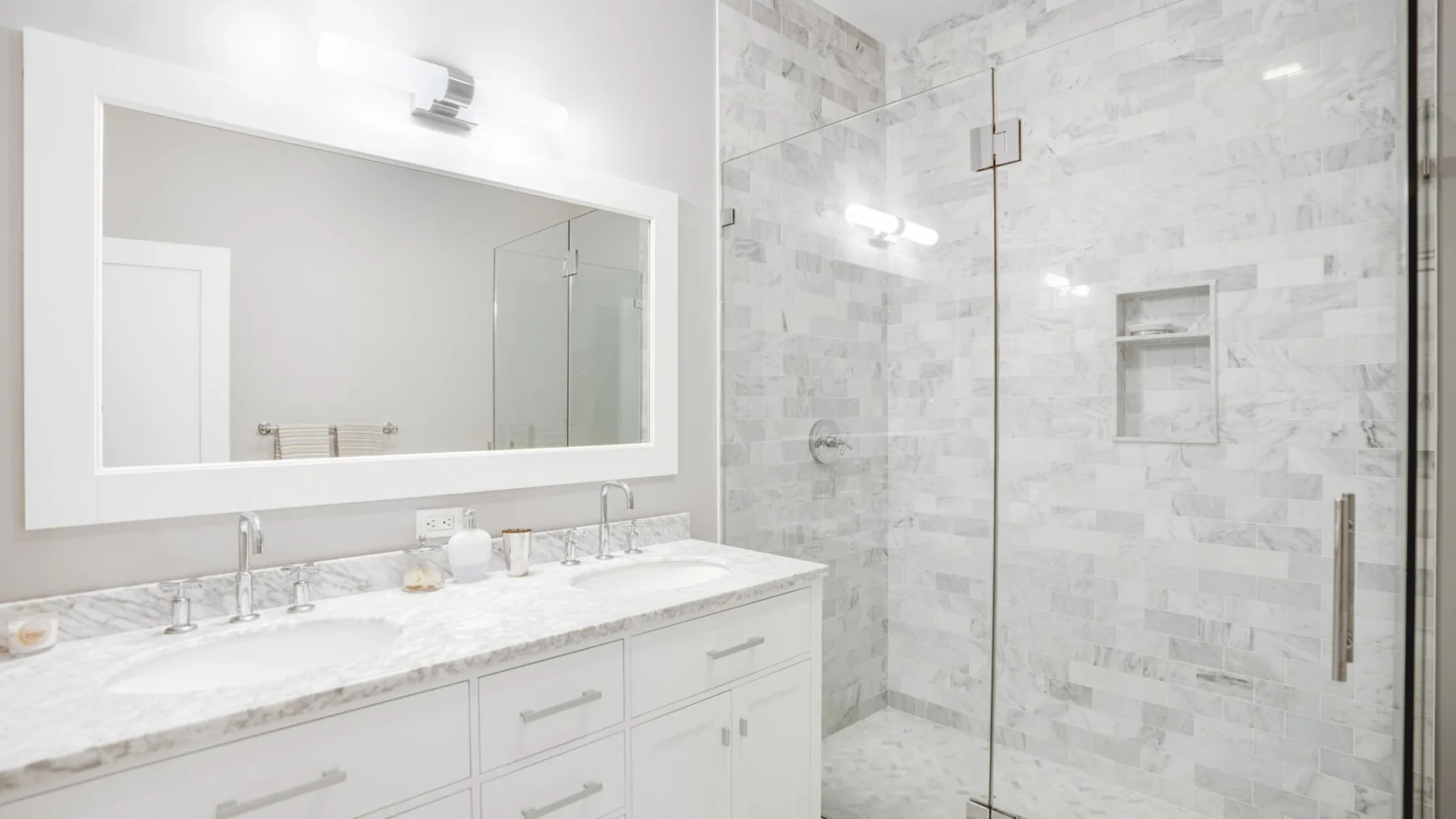 A bright bathroom with a double vanity and a tiled shower.