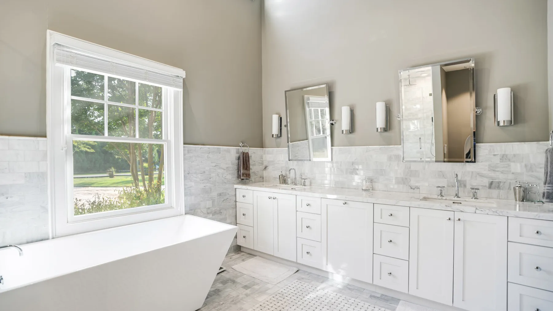 A bright bathroom with a bathtub, white cabinetry, and a large window.