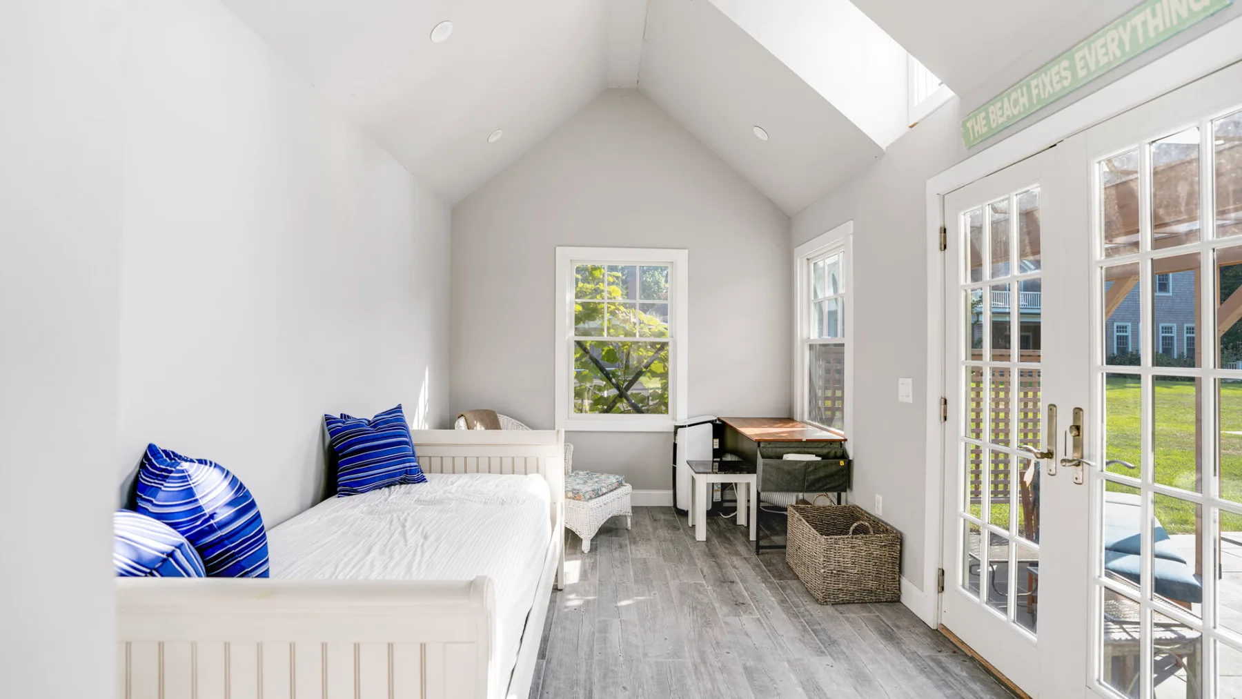 A bright bedroom with beds, a desk, and glass doors opening to a patio.