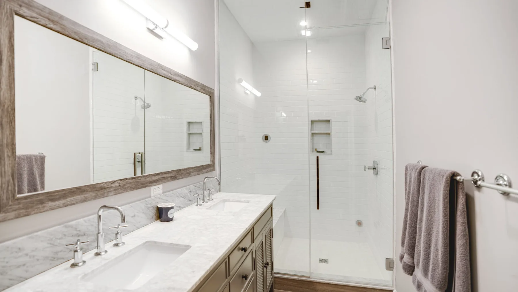 A bright bathroom with a long vanity, mirror, and glass shower.