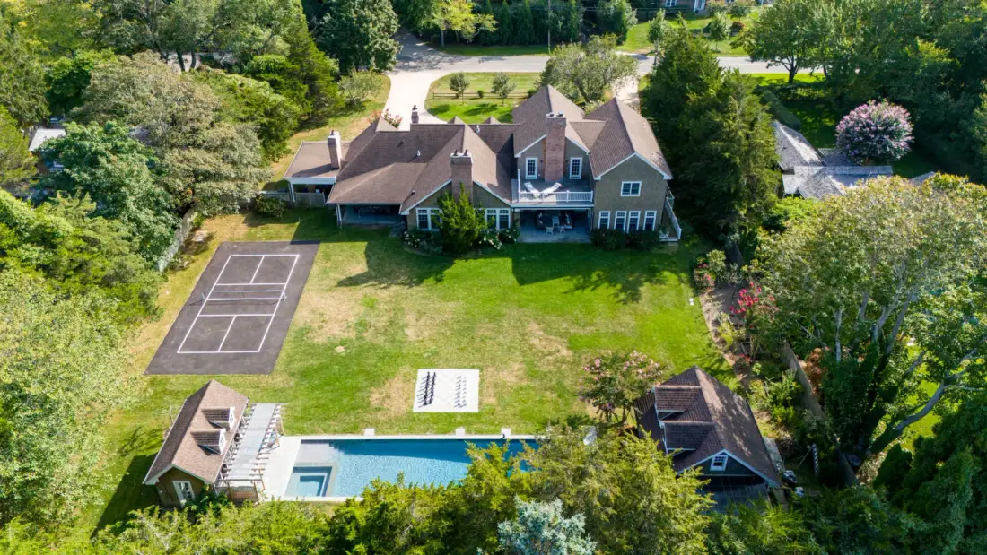 Vista aérea de una casa y sus jardines, con piscina y cancha de tenis.