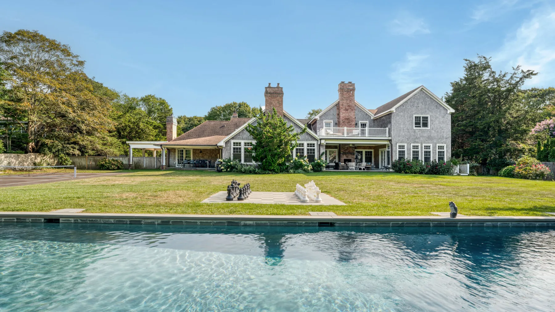 A large house overlooks a swimming pool and broad green lawn.