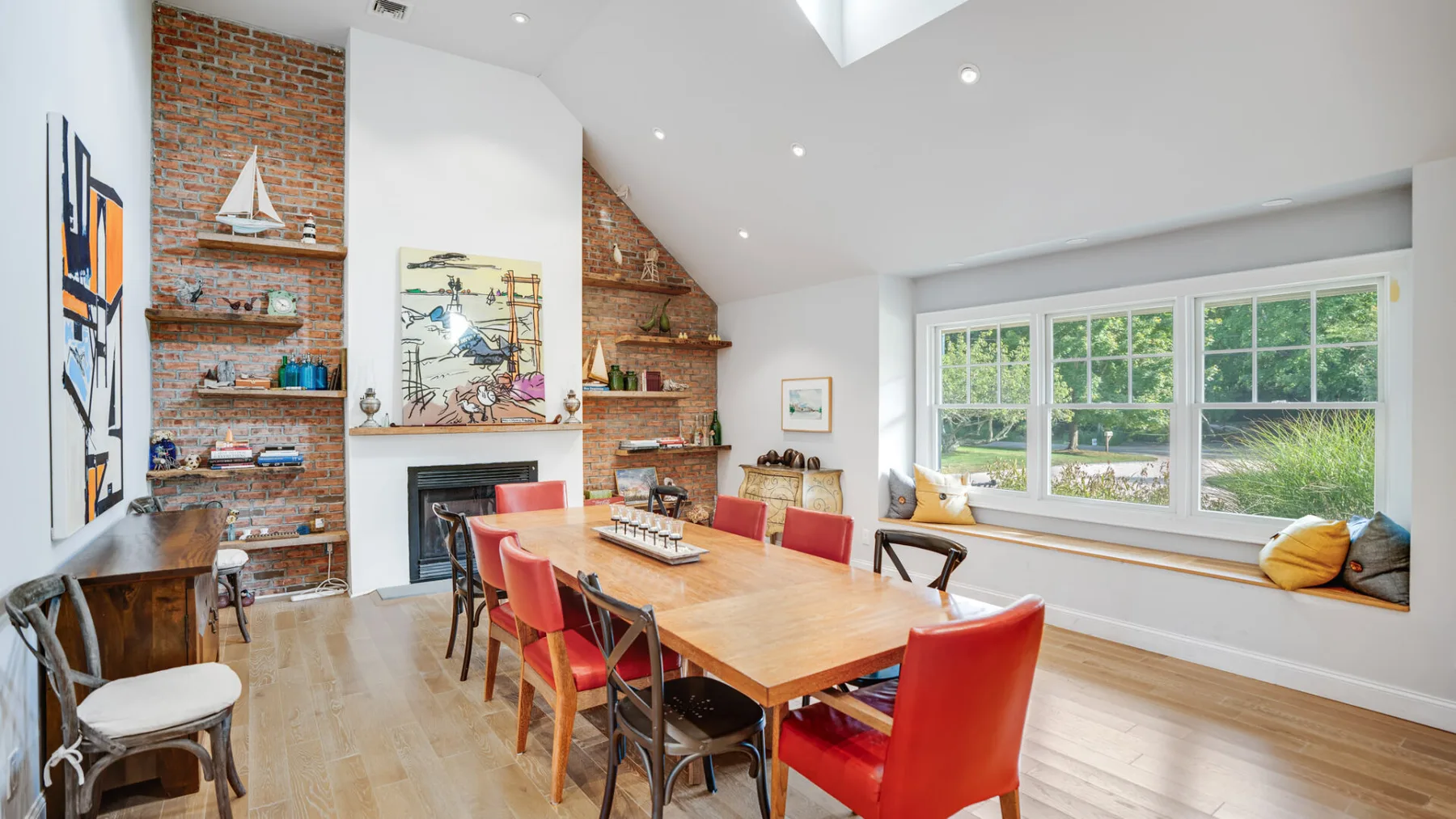 A bright dining room with a long wooden table beside large windows.