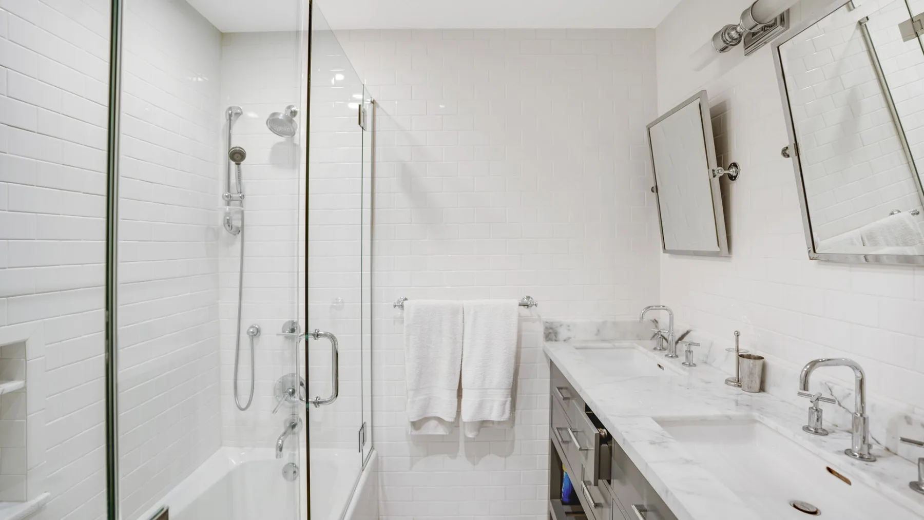 A bright tiled bathroom with a glass shower and a long vanity.