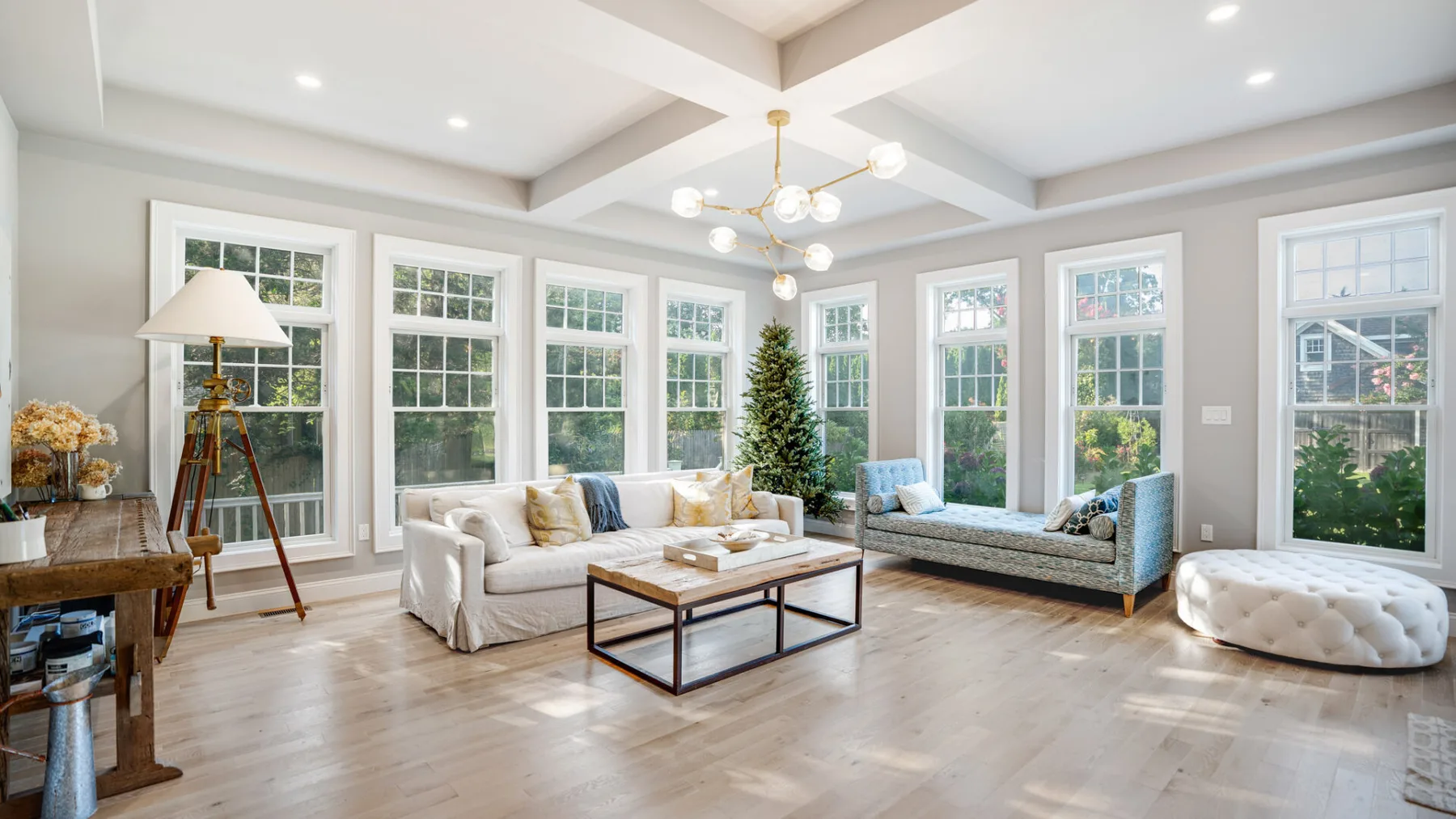 A bright living room with seating arranged around a coffee table and a decorated tree.