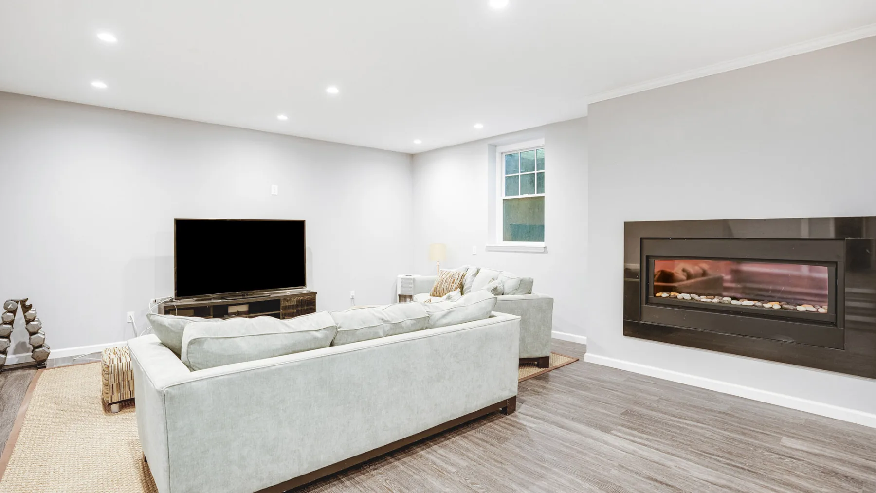 A bright living room has pale seating, a television, and a fireplace.