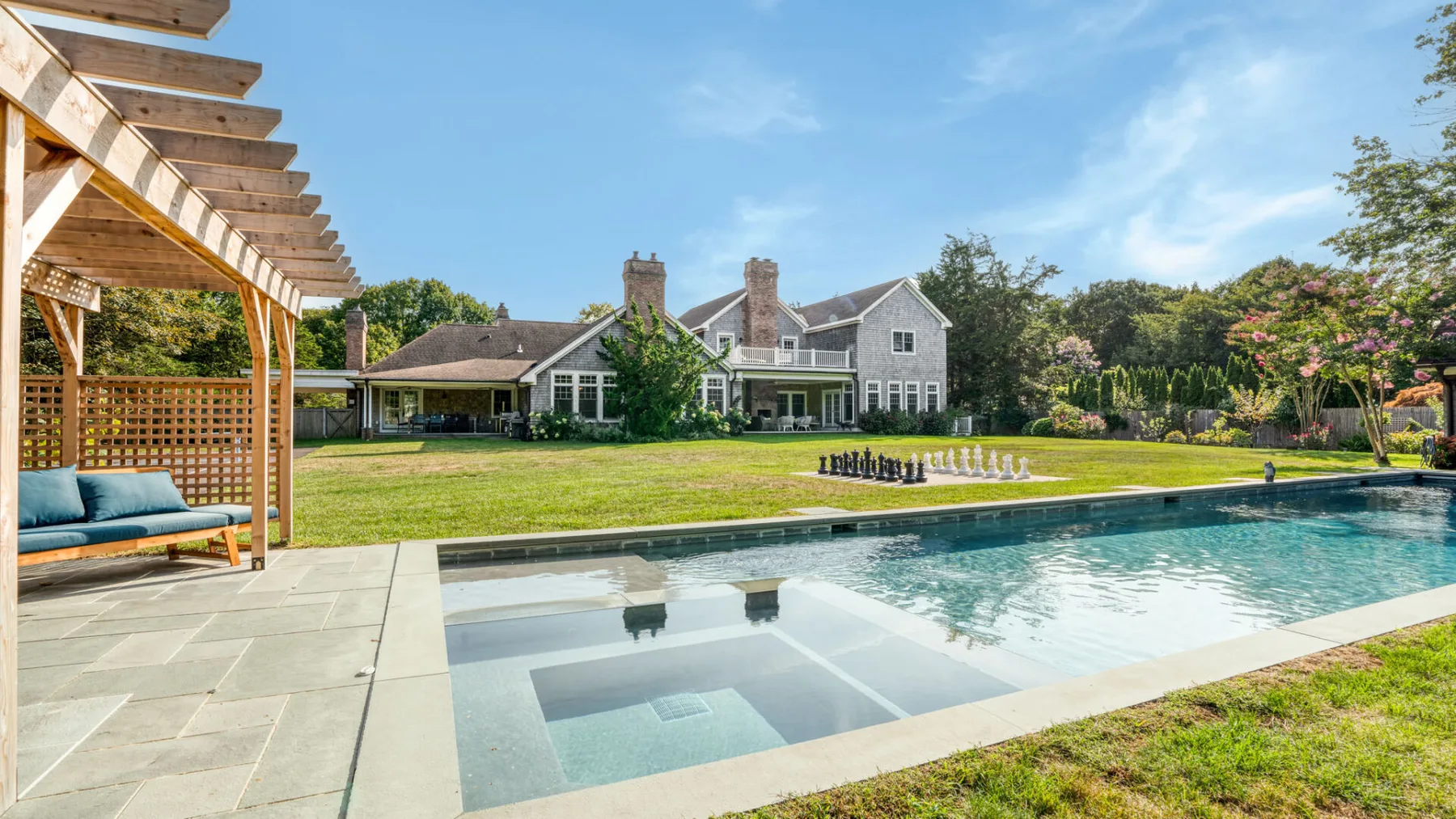 Un patio ajardinado con una piscina y una casa grande al fondo.
