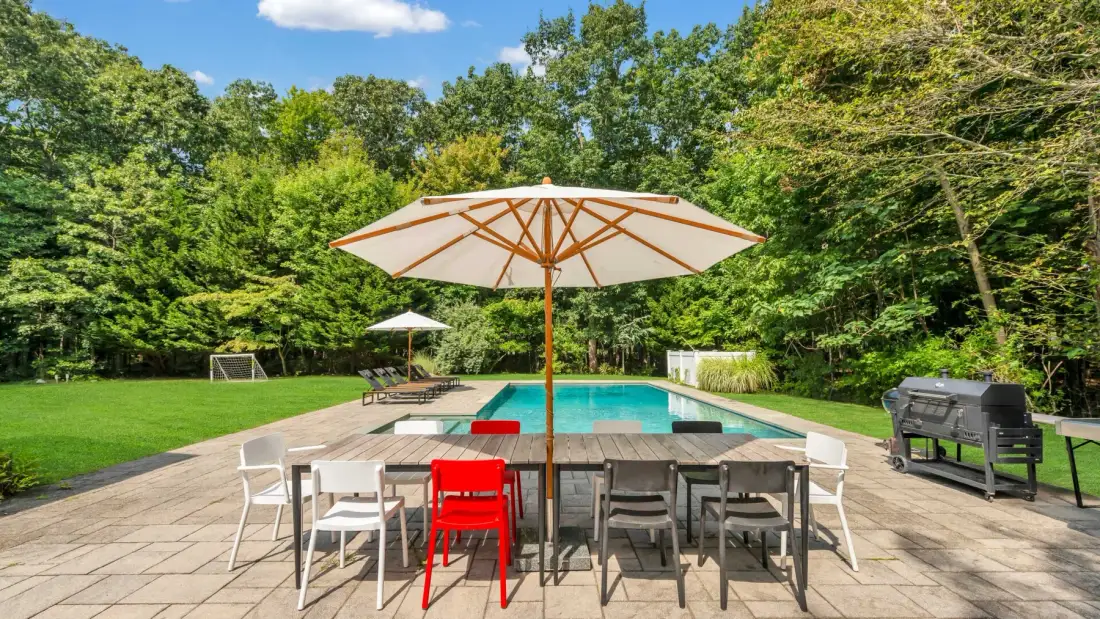 An outdoor pool sits beside a paved patio with tables and seating.