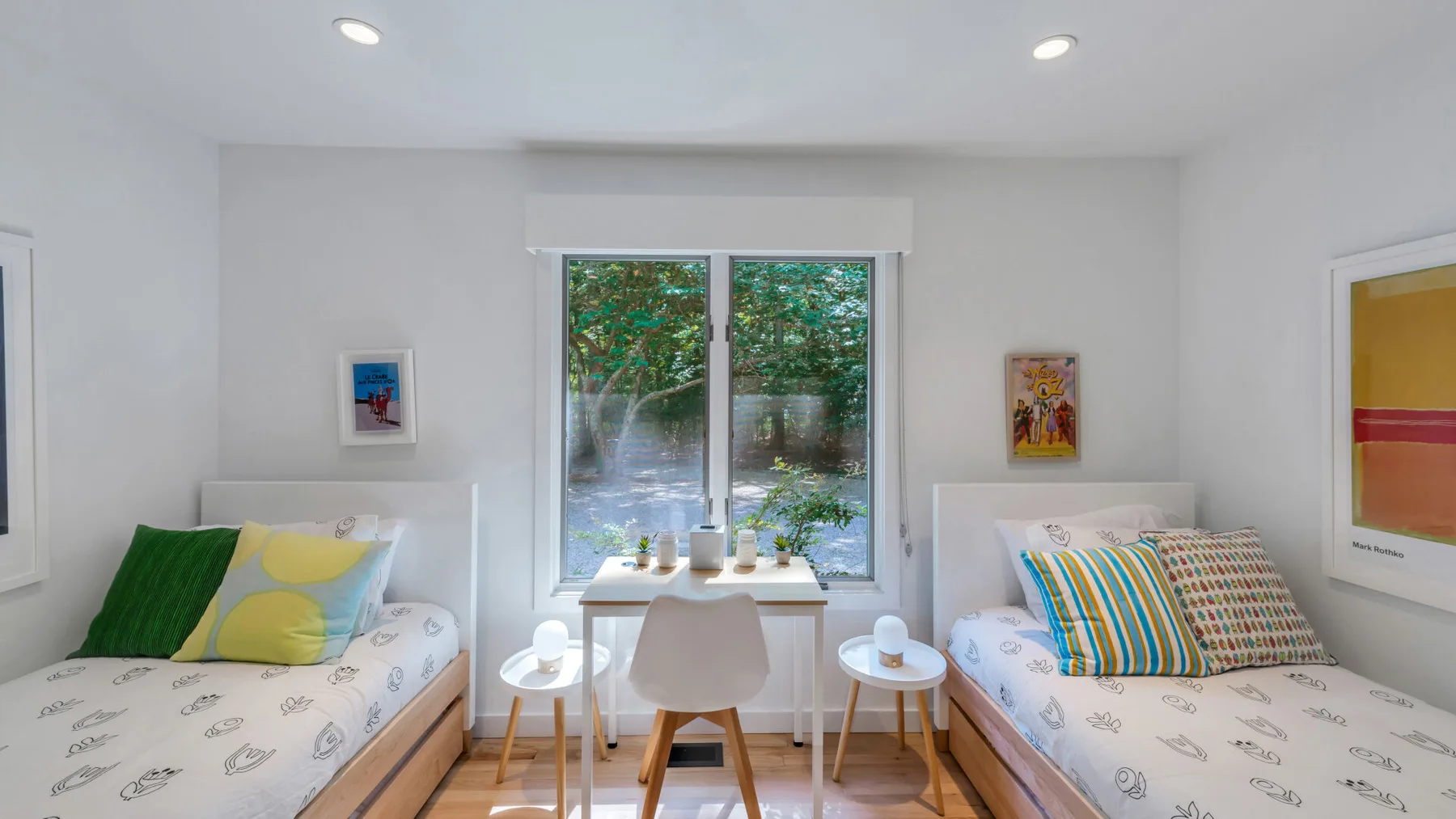 A bright bedroom with two beds and a window overlooking greenery.