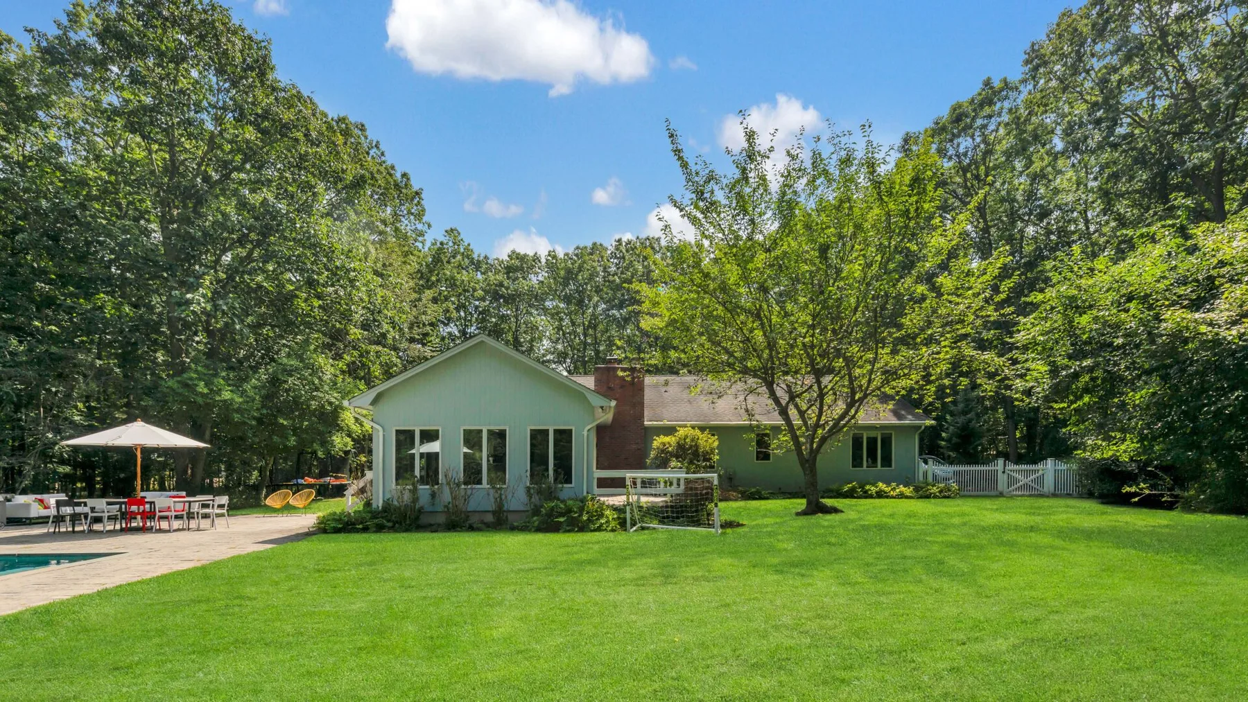A light-colored house sits beside a broad green lawn and leafy trees.