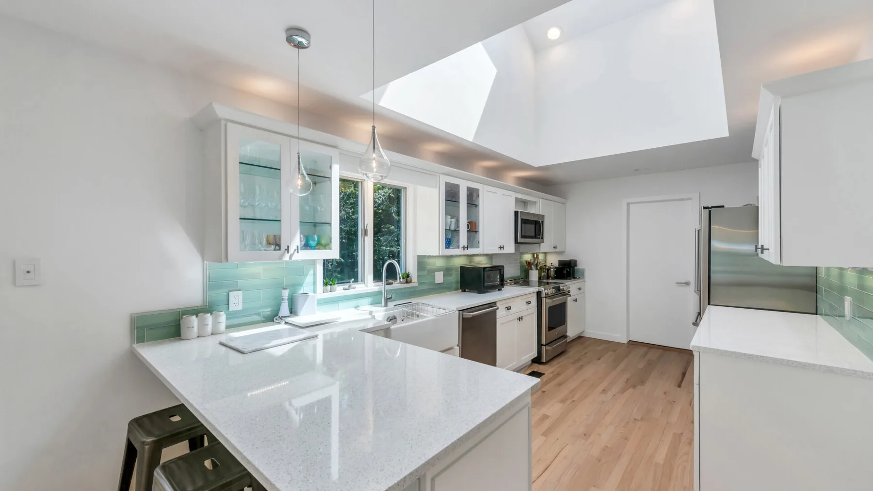 A bright modern kitchen with a white island and green backsplash.
