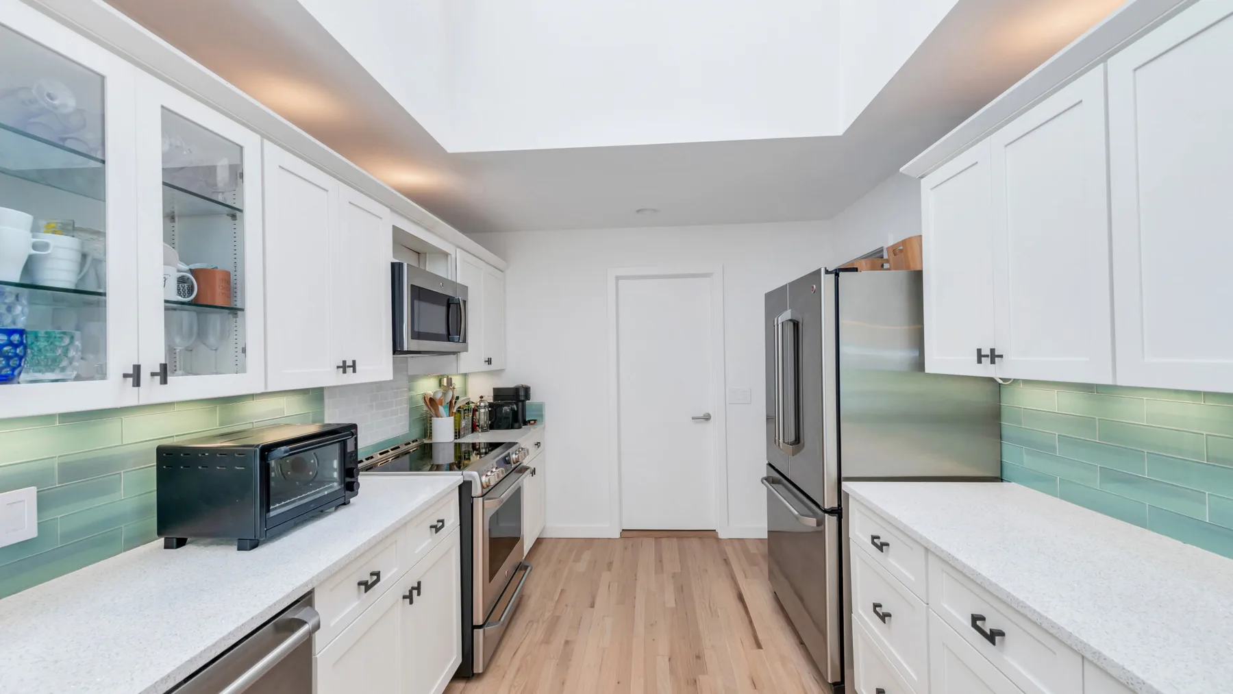 A bright kitchen with white cabinets, stainless steel appliances, and wood flooring.