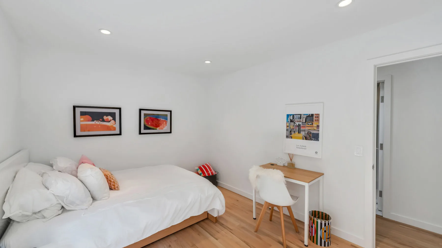 A bright bedroom with a bed, wall art, and a small desk.