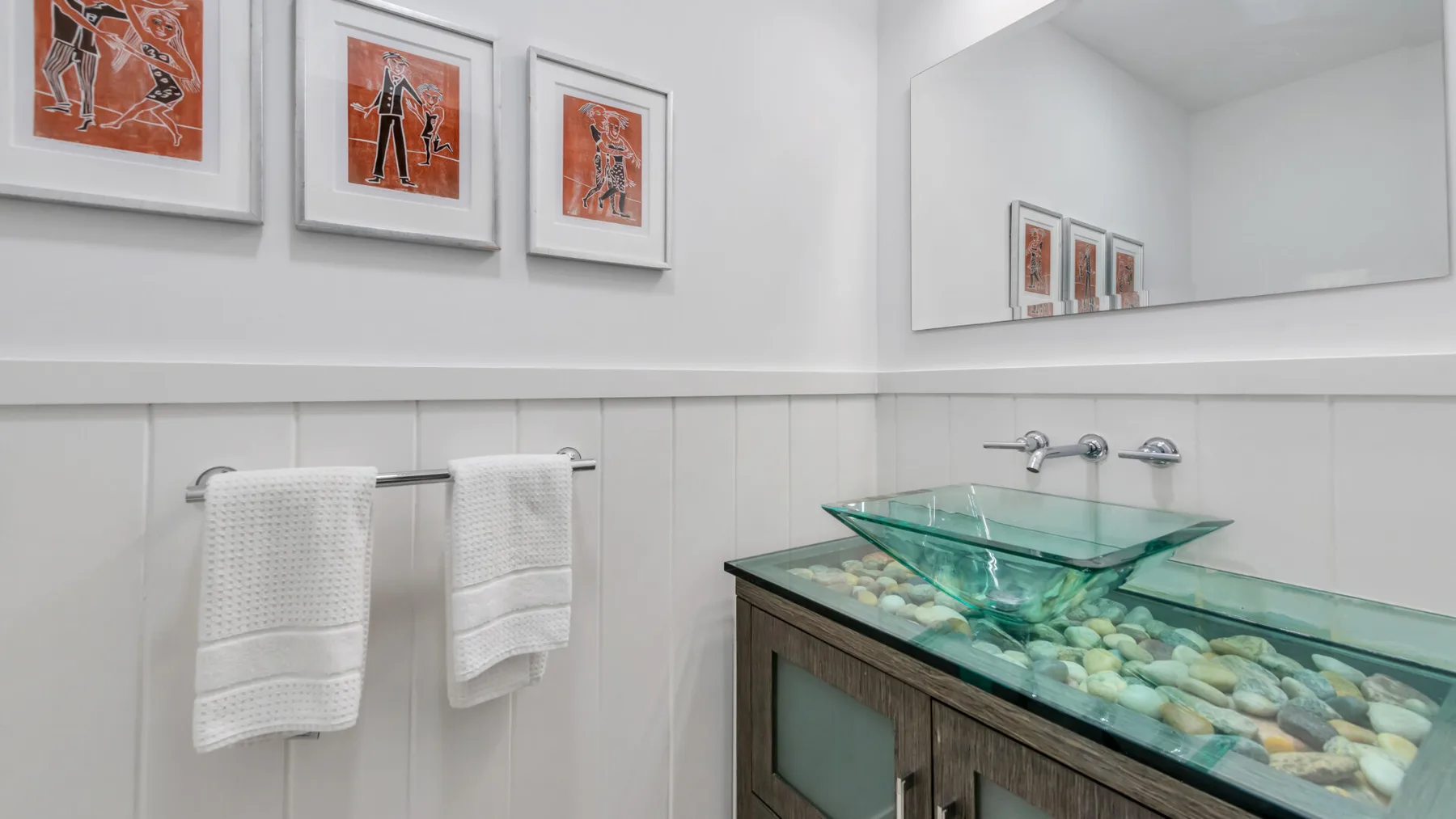 A bathroom vanity with a glass vessel sink, towels, and framed artwork.