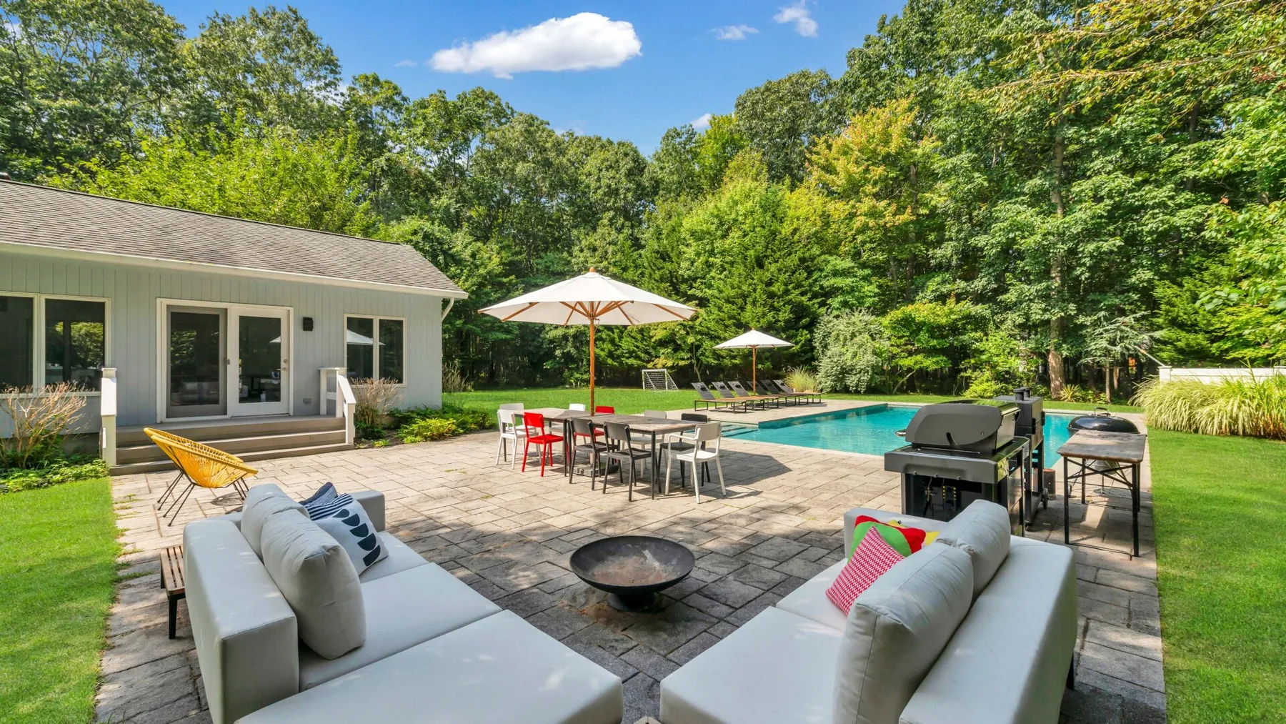 A patio with outdoor seating, an umbrella, and a swimming pool beside a house.