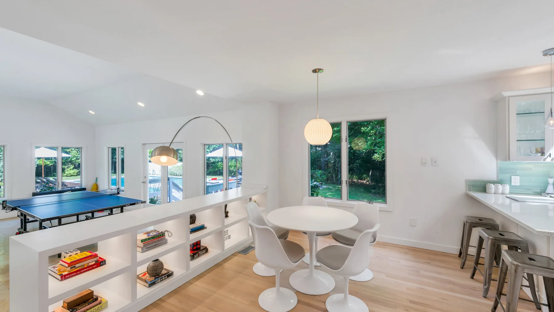 A bright dining area with a round table beside a built-in shelf and windows.
