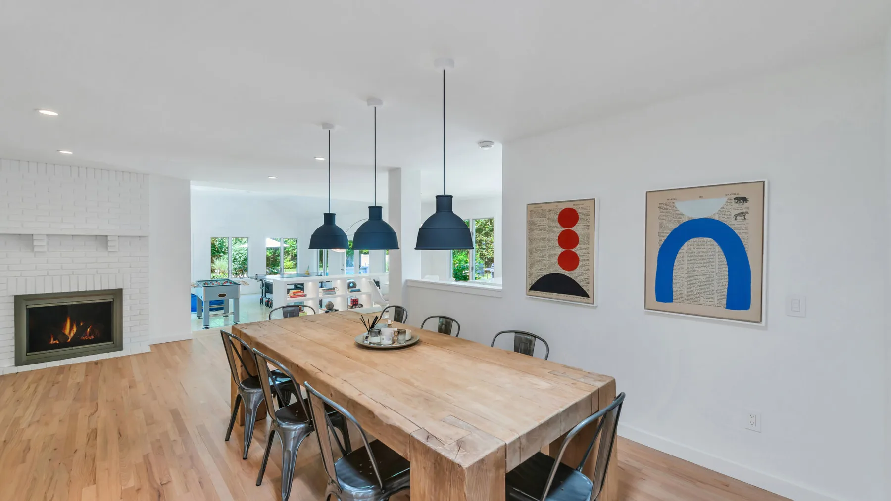A dining area with a long wooden table and pendant lights.