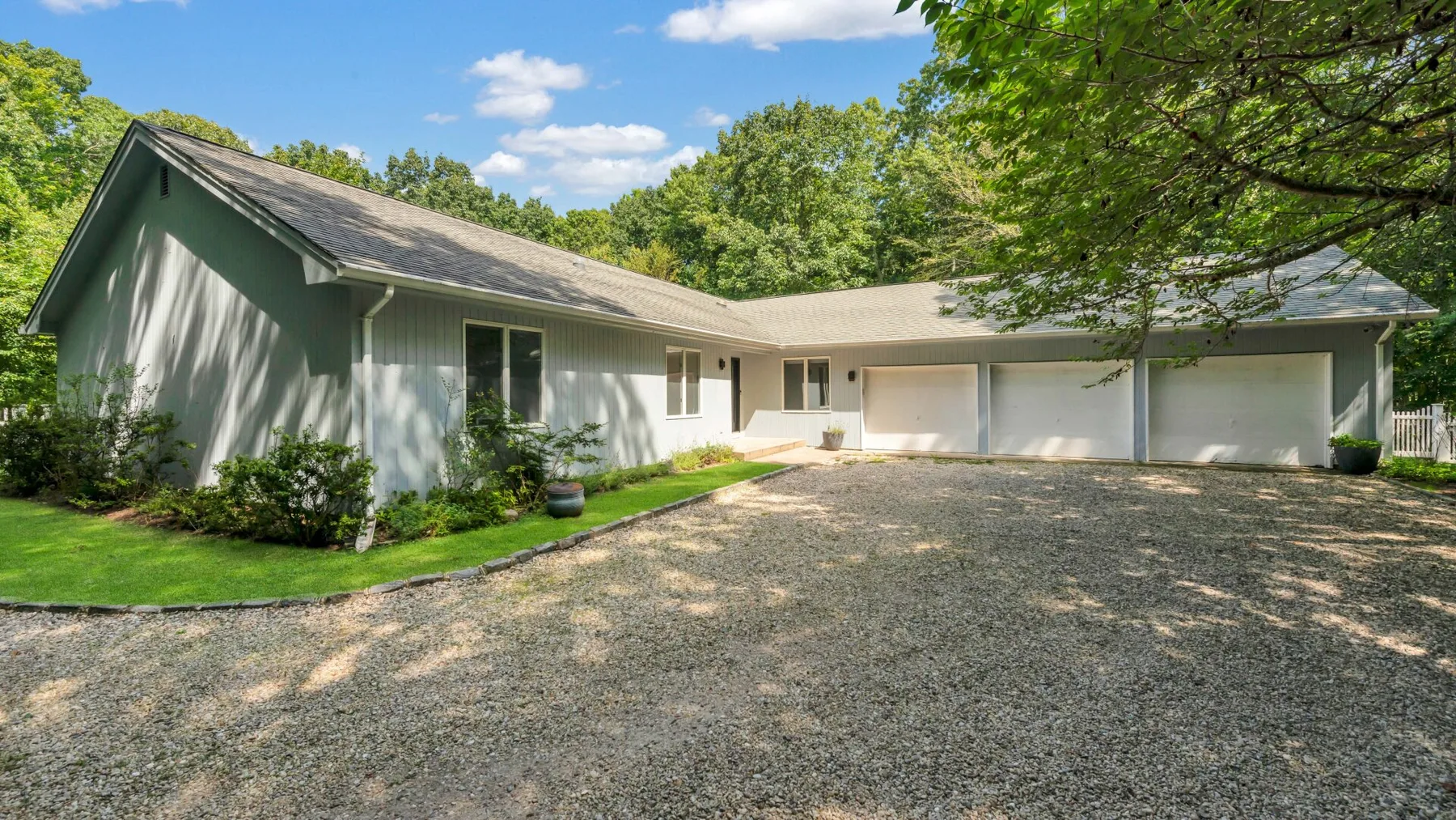 A modern house with a broad gravel driveway surrounded by leafy trees.