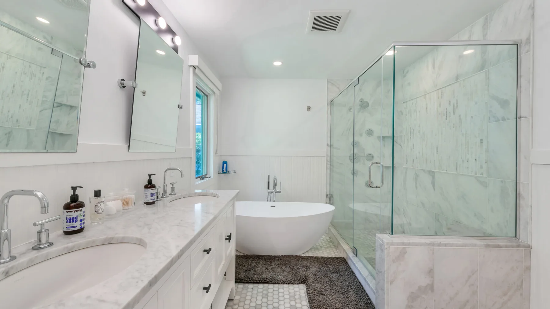 A bright bathroom with a bathtub, glass shower, and long vanity.