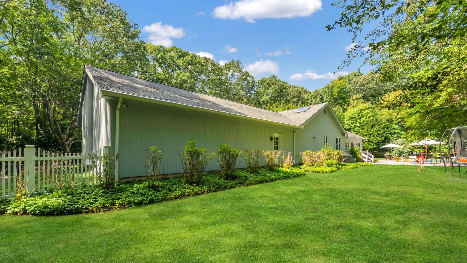 A green building stands beside a broad lawn and leafy trees.