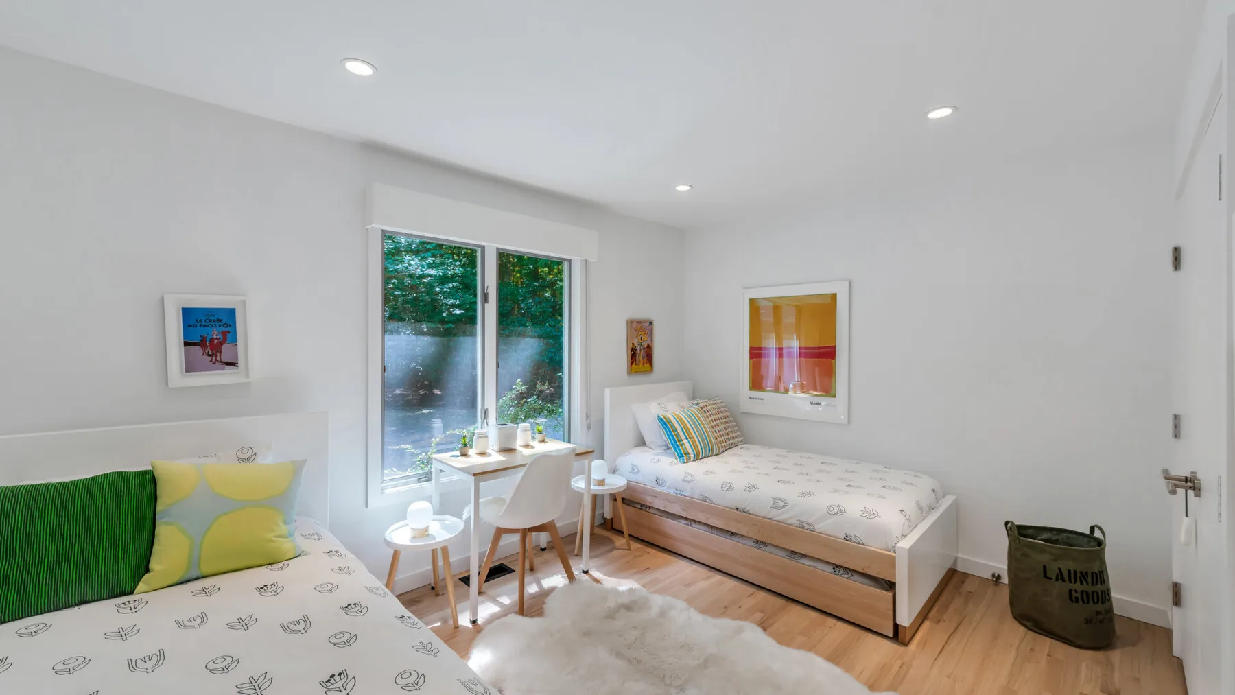 A bright bedroom with two beds, colorful cushions, and large windows.