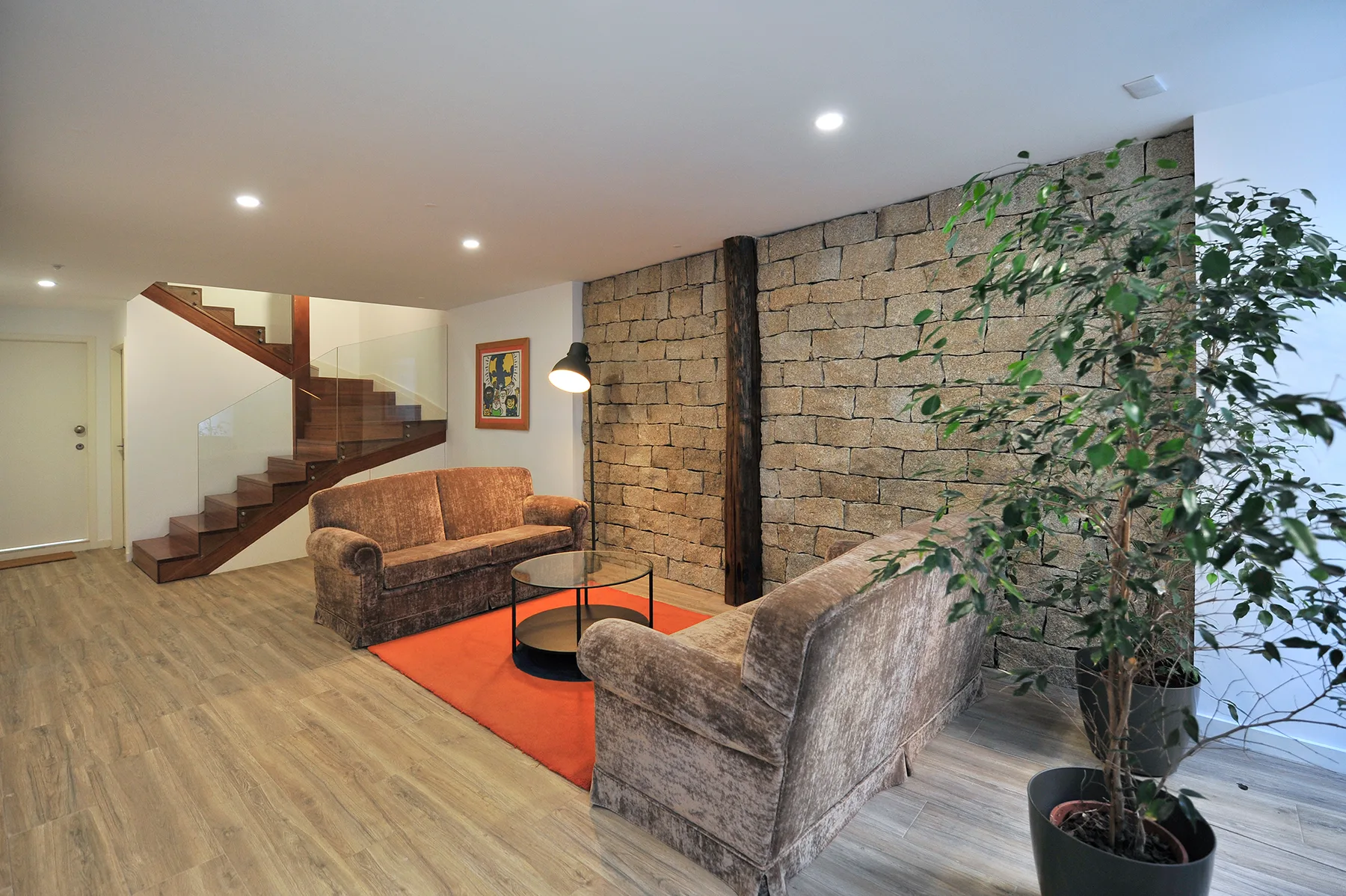 A living room with seating around a low table and a staircase along the stone wall.