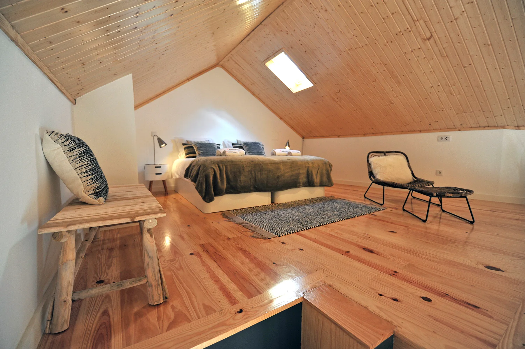 A bedroom with a bed, a wooden bench, and a chair beneath a sloped ceiling.
