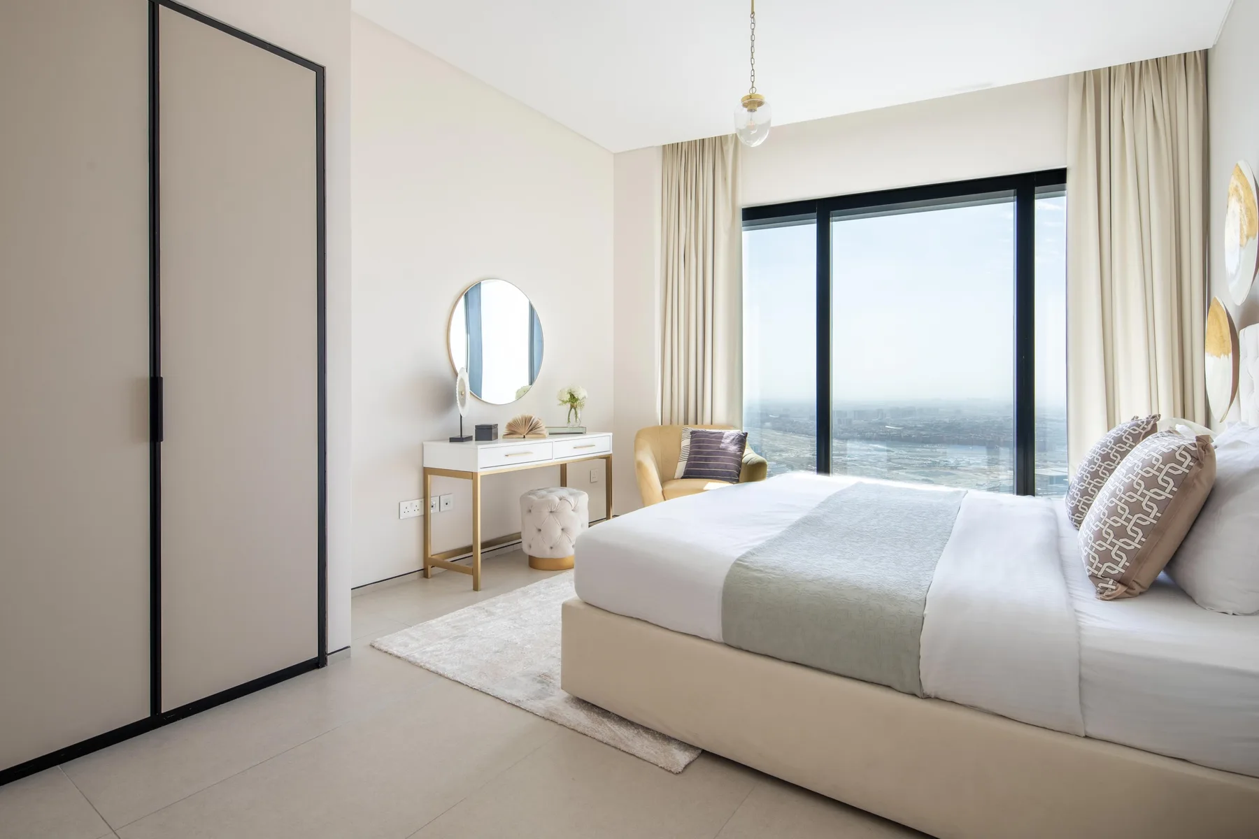 Un dormitorio luminoso con una cama junto a una ventana grande y un tocador.
