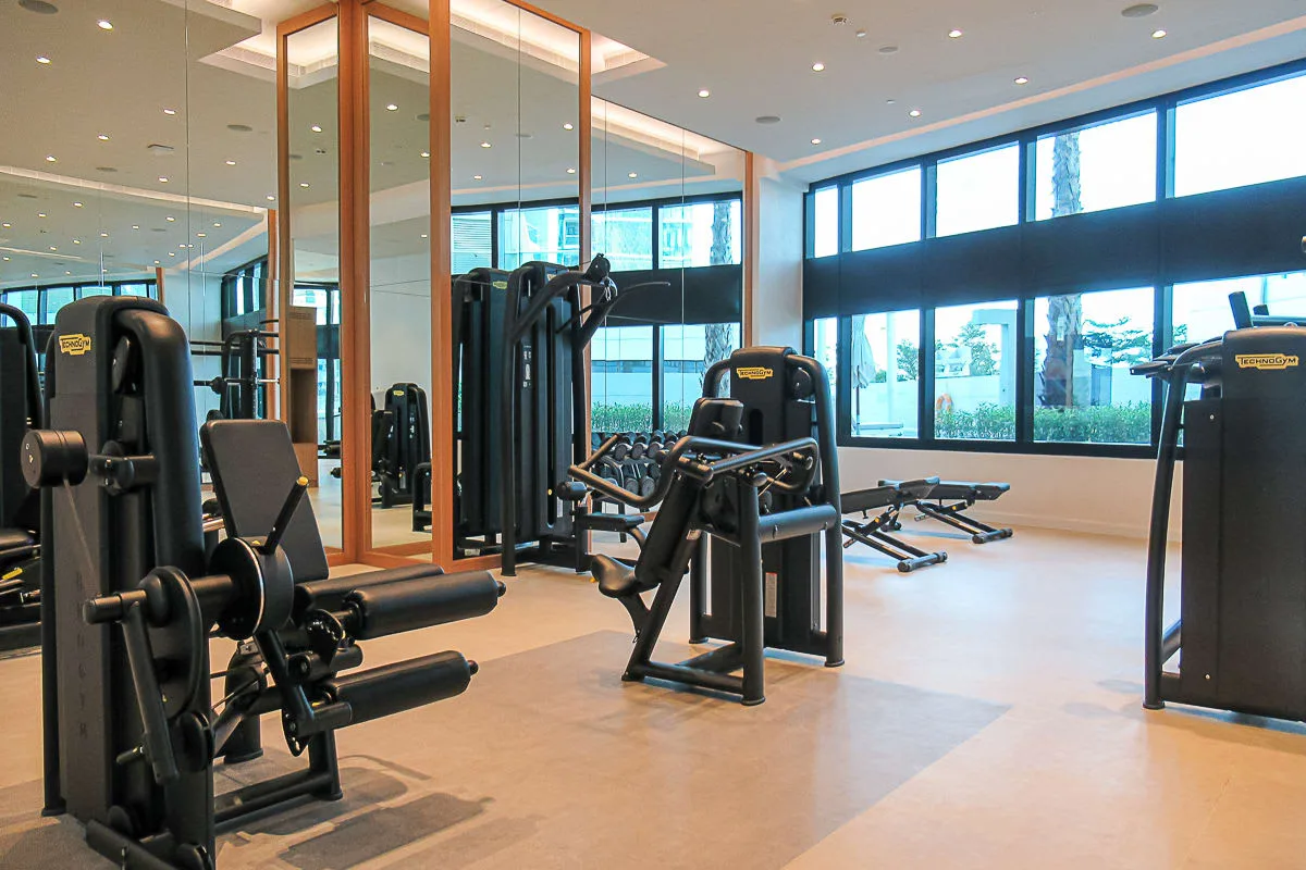 Un gimnasio con máquinas de pesas y grandes ventanas.