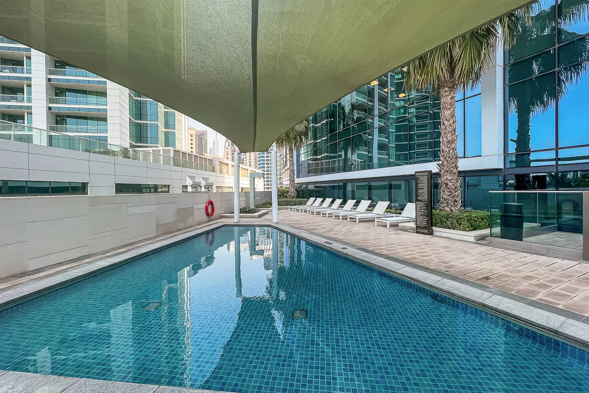 Una piscina al aire libre está junto a edificios con fachadas de vidrio y tumbonas.