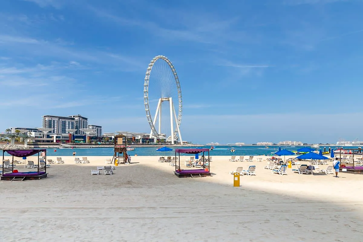 Una playa de arena con sombrillas y una gran noria junto al agua.