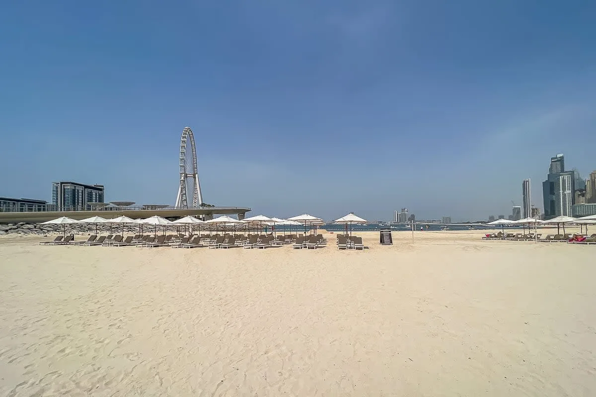 Una amplia playa de arena con filas de sombrillas y edificios urbanos en el horizonte.