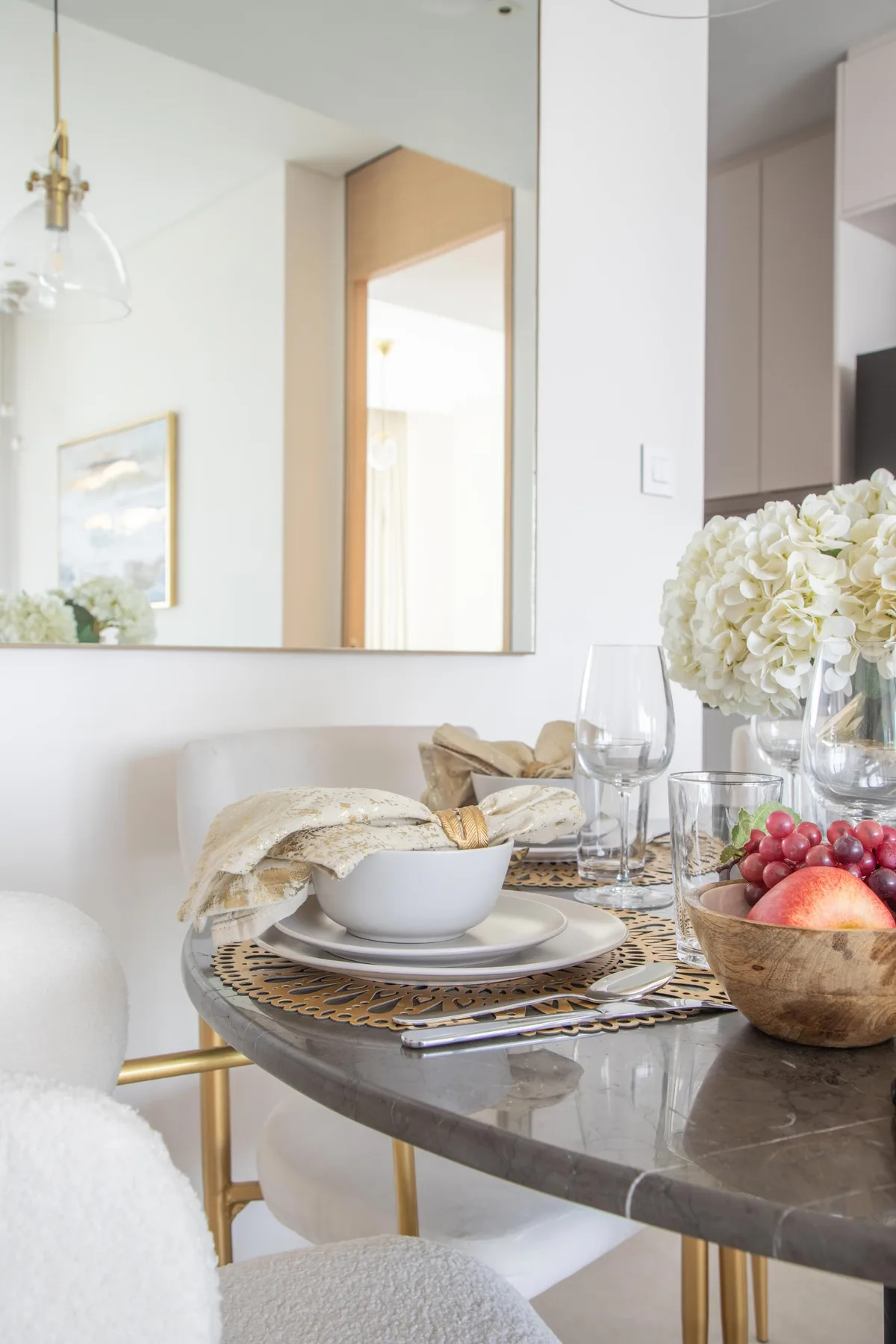 Un comedor con la mesa puesta, flores y un gran espejo de pared.
