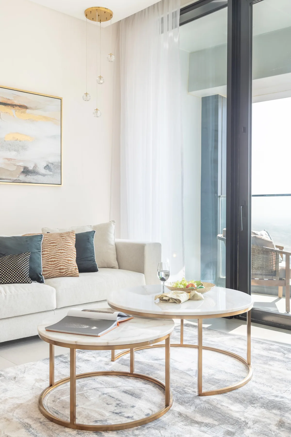 A bright living room with seating, round coffee tables, and tall windows.