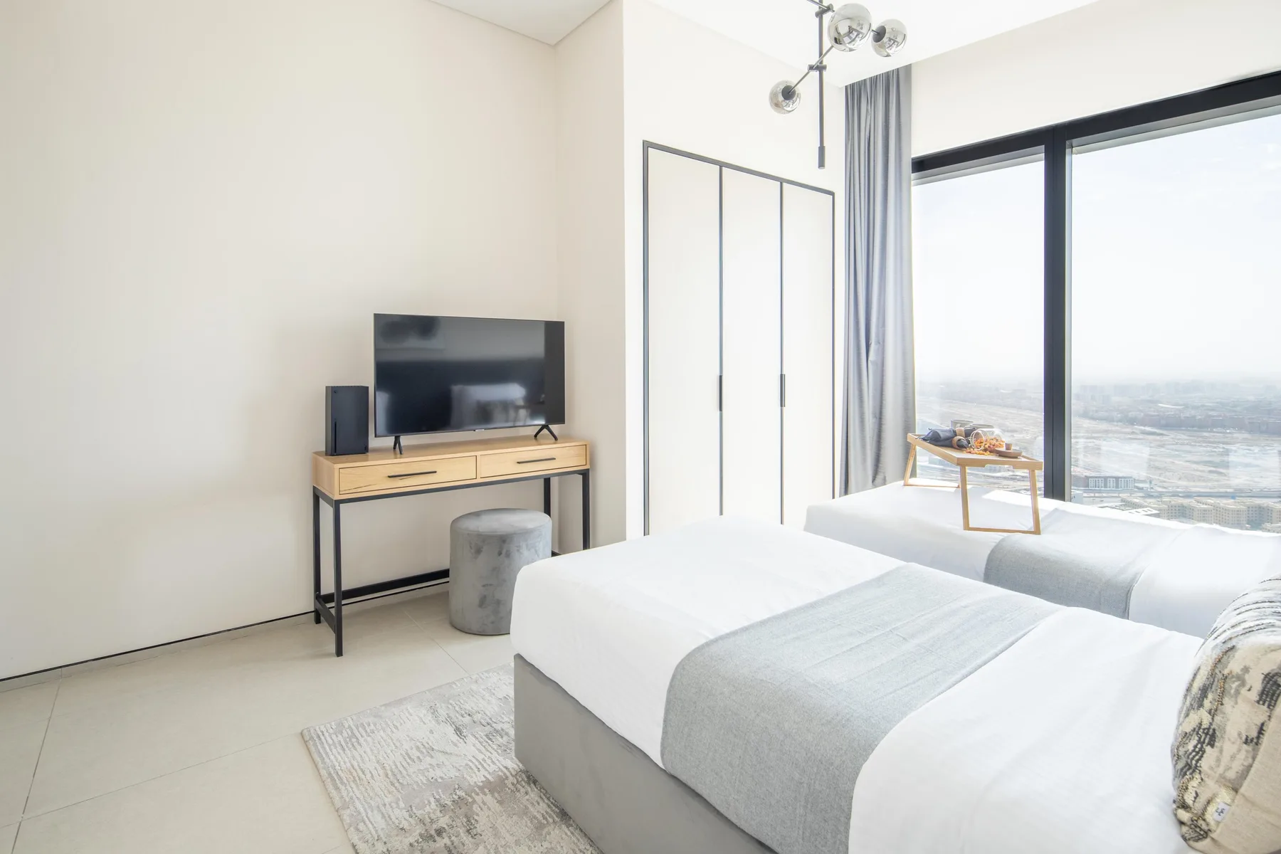 Un dormitorio luminoso con una cama junto a una ventana grande y un televisor.