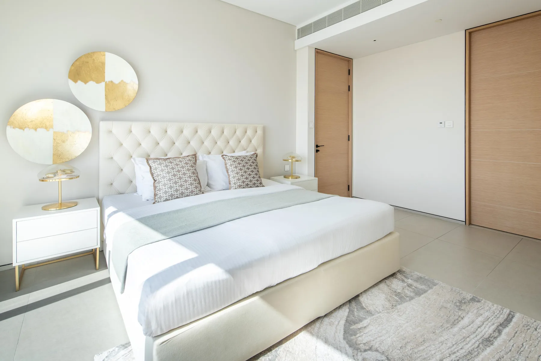 Un dormitorio luminoso con una cama grande, mesitas de noche y arte circular en la pared.