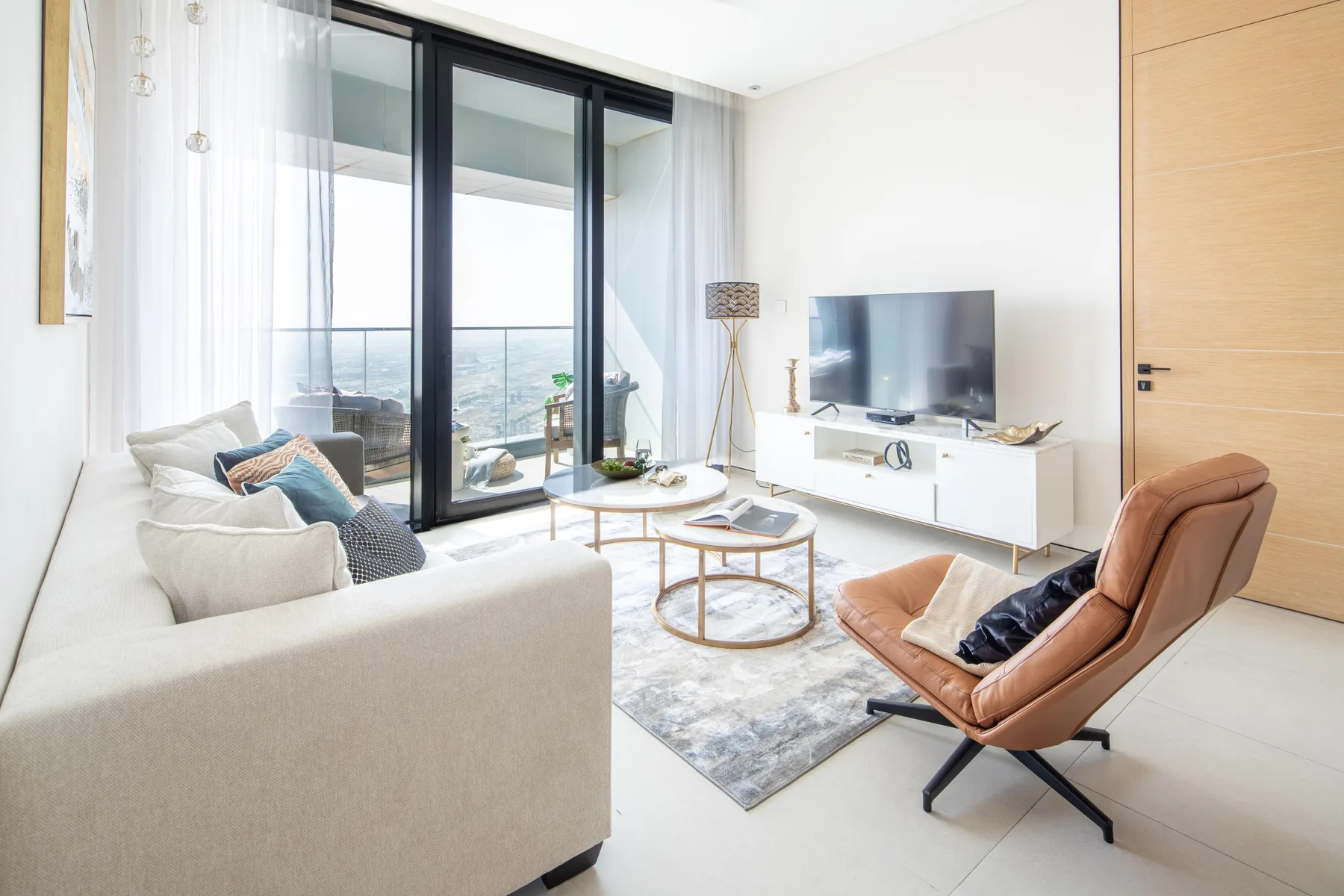 A bright living room with a seating area, coffee tables, and a television.