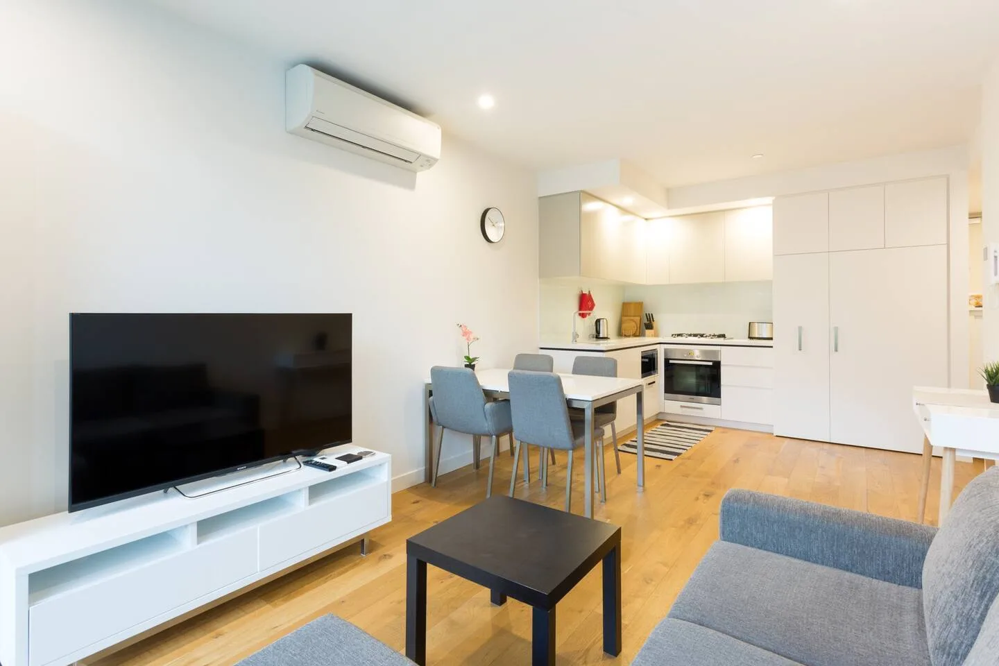Una luminosa sala-comedor con televisor, mesa y cocina abierta.
