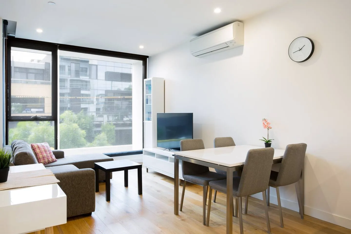 Una luminosa sala de estar y comedor con grandes ventanas y un televisor.