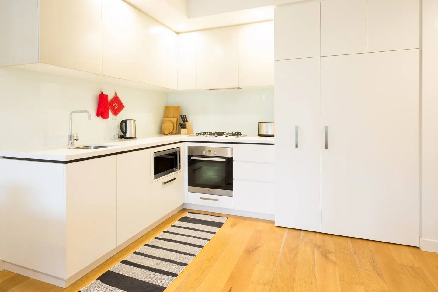 Cocina blanca y luminosa con fregadero, electrodomésticos sobre la encimera y aparatos de cocción integrados.
