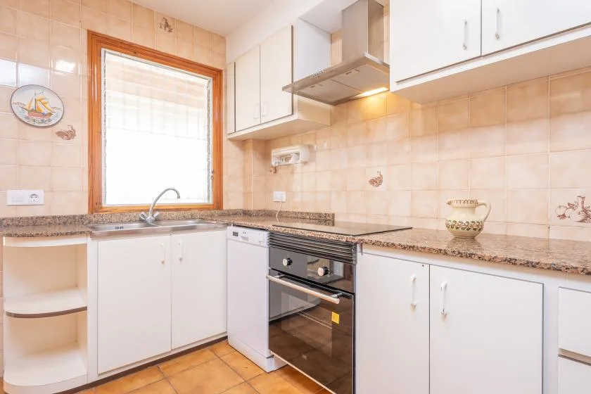 A tiled kitchen with white cabinets, a sink, and an oven.