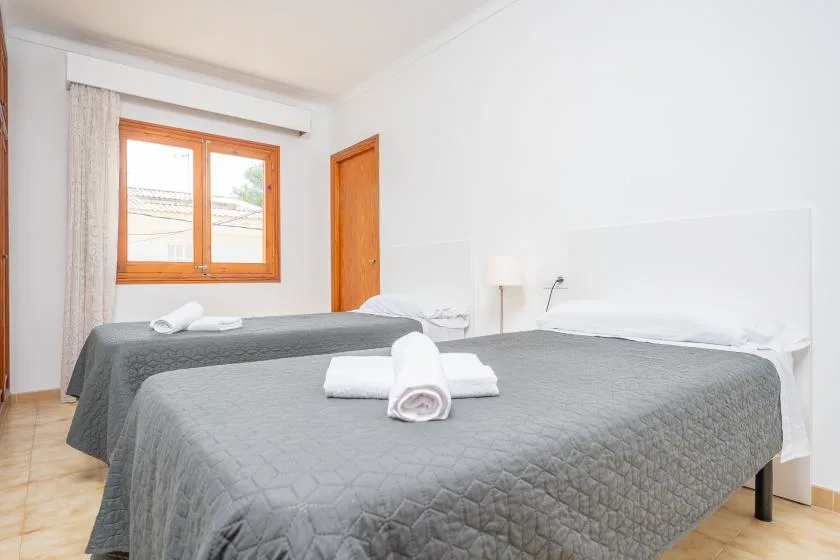 A bedroom with two beds covered in gray bedspreads and folded white towels.