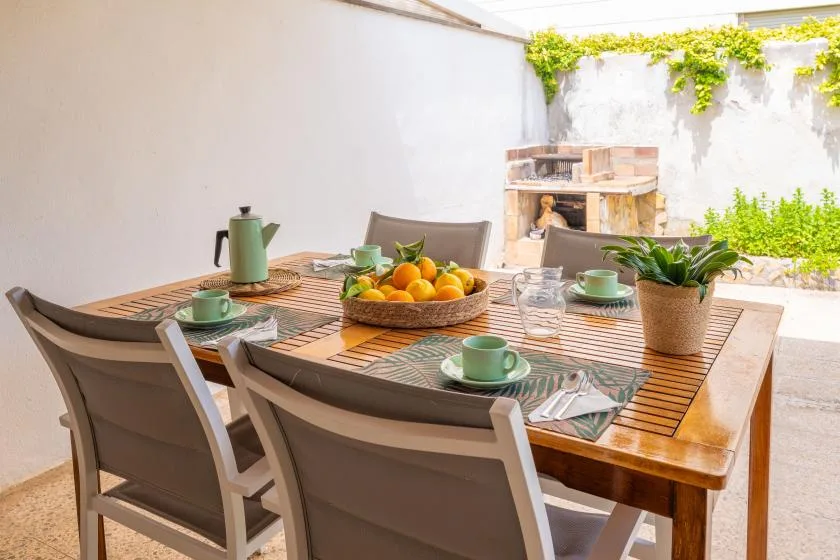 An outdoor dining area with a wooden table set with dishes and fruit.