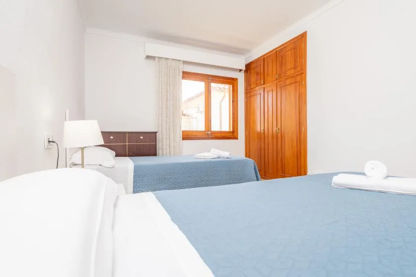 A bedroom with two beds, a window, and a wooden wardrobe.