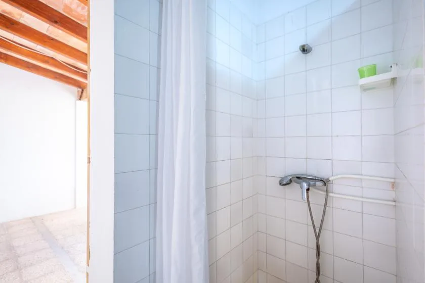 A tiled bathroom shower area with a white curtain and wall-mounted showerhead.